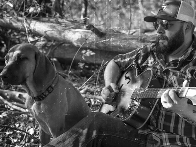 Jesse Quandt sitting with his guitar and his dog right beside him
